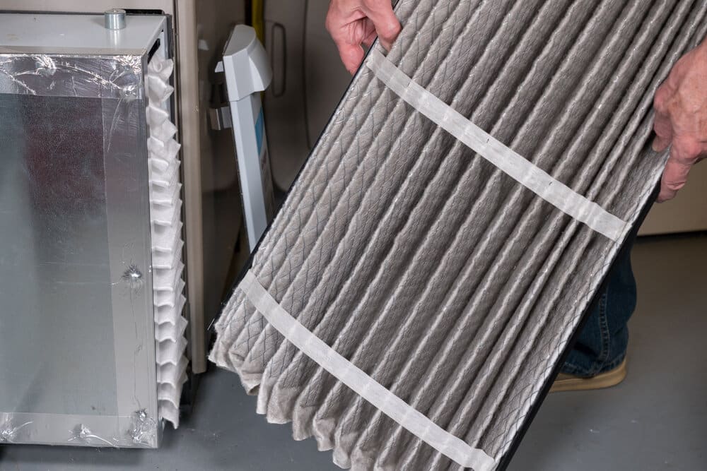 Senior man examining a folded dirty air filter in the HVAC furnace system in basement of home