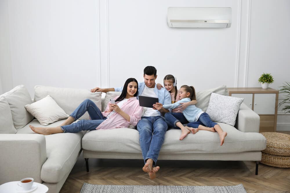 Happy family resting under air conditioner on white wall at home