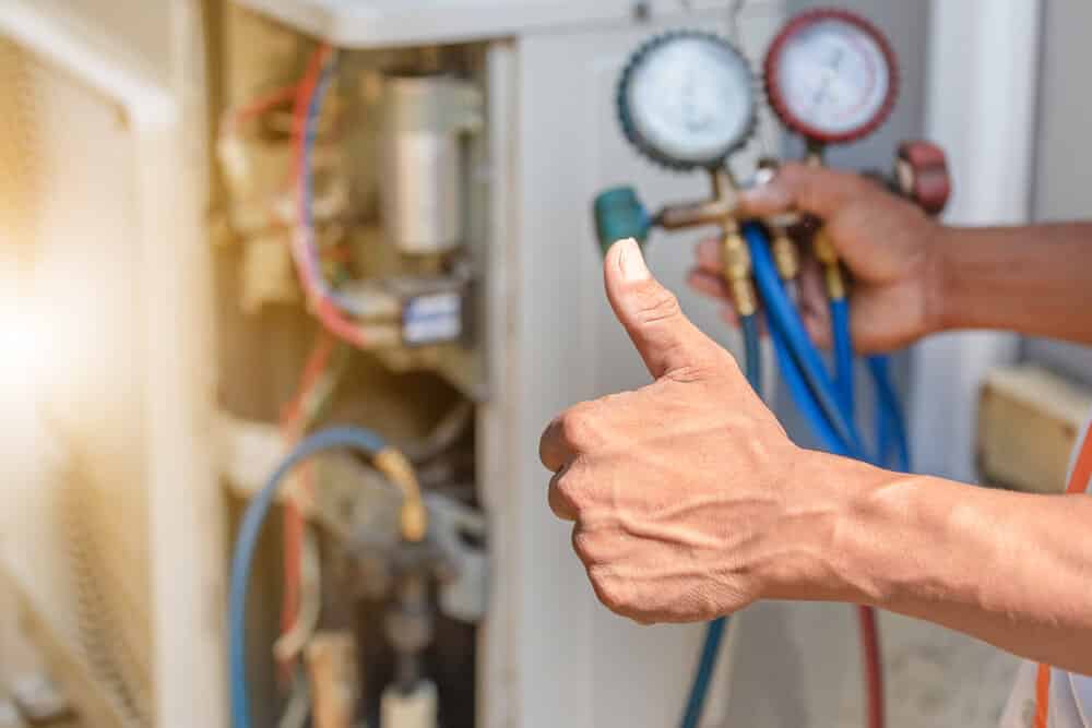 Close up of thumbs up in front of repairman fixing HVAC system
