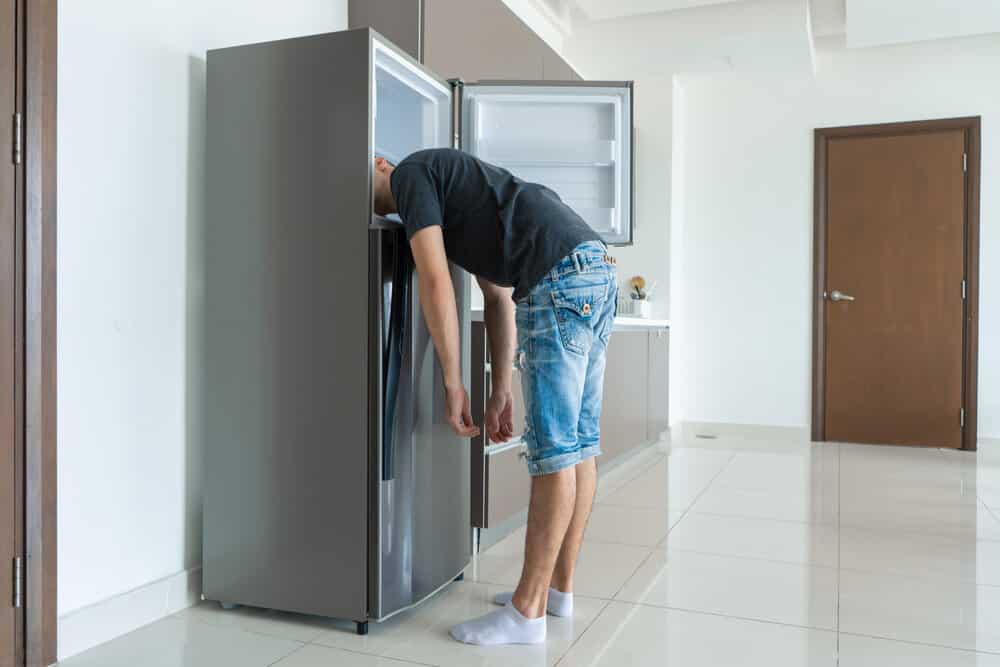 On a hot day, the guy cools with his head in the refrigerator. Broken air conditioner.